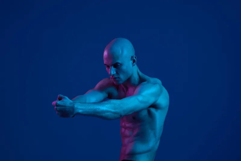 Athletic man posing in a creative studio with dramatic lighting, showcasing strength and fitness. The image features a striking blue color scheme, adding depth and intensity.