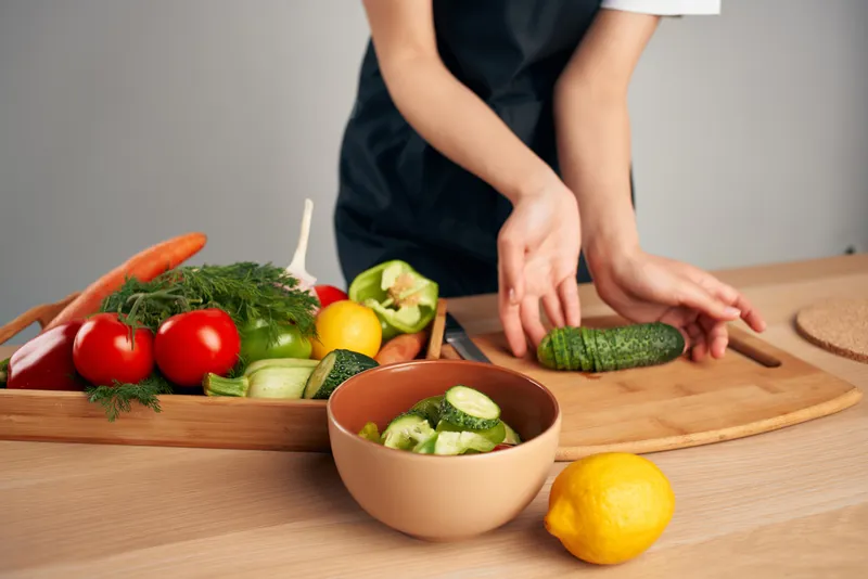Женщина в черном фартуке нарезает овощи на кухне, готовит еду