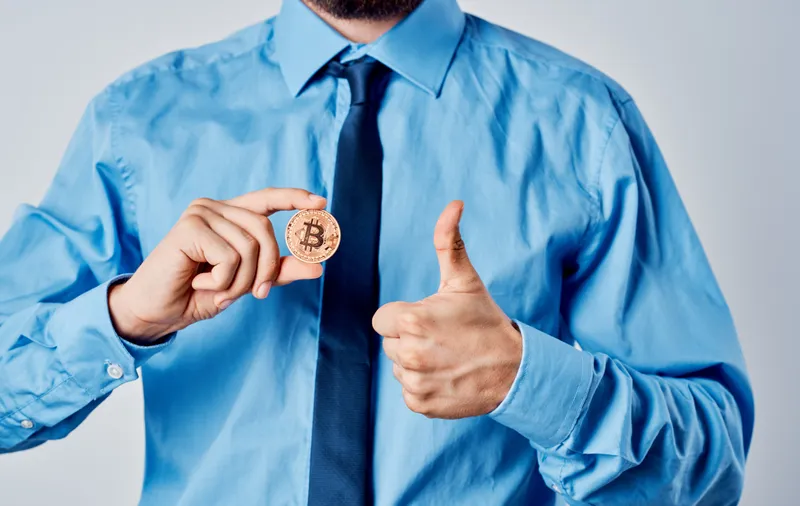 Деловой мужчина в синей рубашке с монетой в руке, криптовалюта Bitcoin, финансовая модель