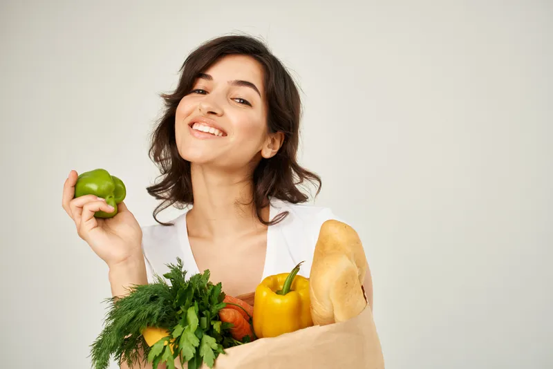 Весёлая брюнетка с пакетом продуктов в супермаркете, крупный план