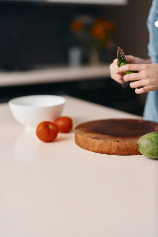Свежесть и здоровье: женщина на кухне нарезает вкусные фрукты на деревянной доске с радостным выражением лица на ярком фоне