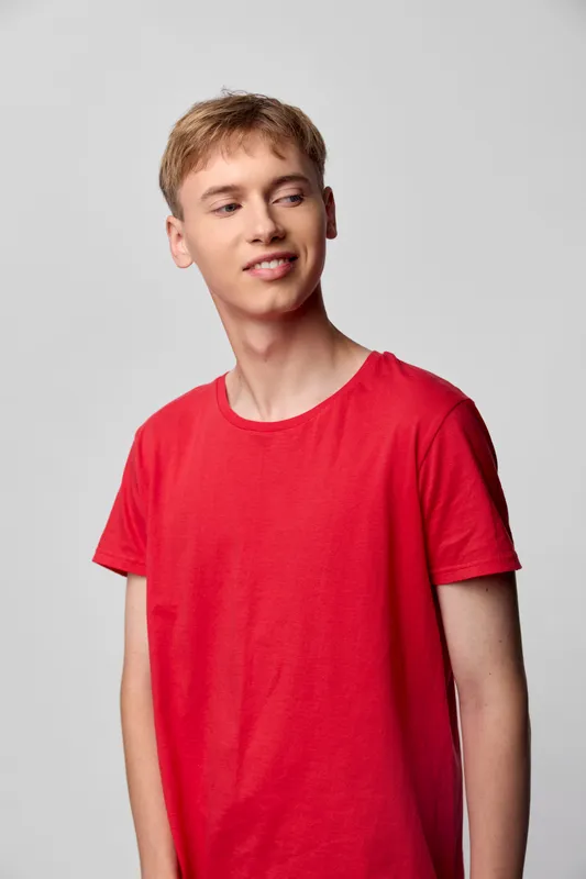 Young man wearing a red t shirt with a relaxed smile, casual studio pose, simple background and soft lighting, showcasing everyday fashion and a confident, approachable vibe