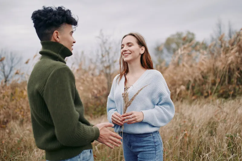 Authentic moment in a autumn field as two friends converse naturally, warm knitwear, gentle light, candid posture, sincere interaction, conveying credibility and trust.