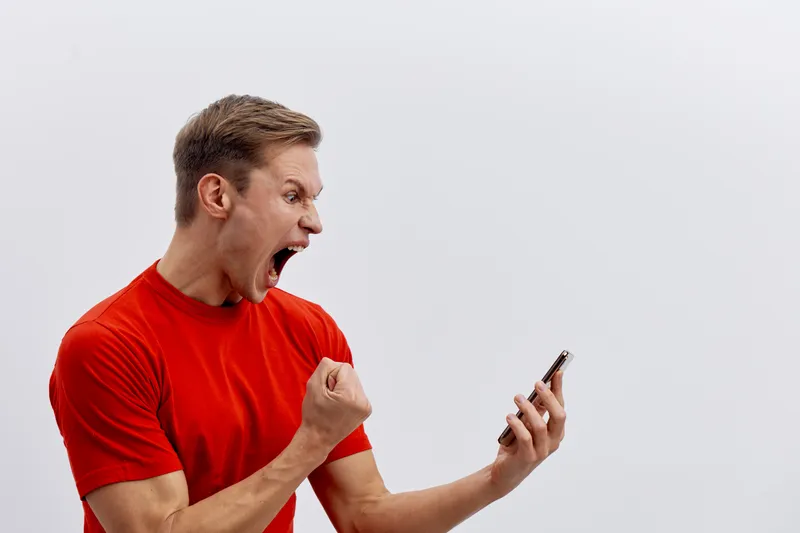 angry man with smartphone shouting wearing red t-shirt isolated on light background digital detox frustration concept