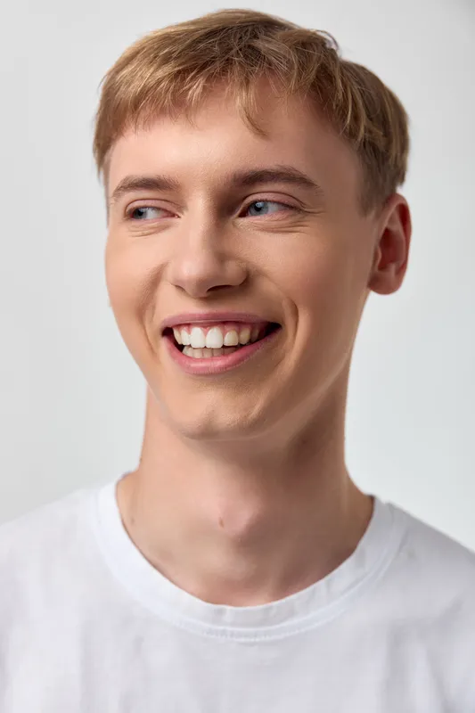 Smiling man in a white t shirt looking off to the side, a candid moment of casual confidence and happiness suitable for lifestyle, fashion, or advertising visuals in studio light