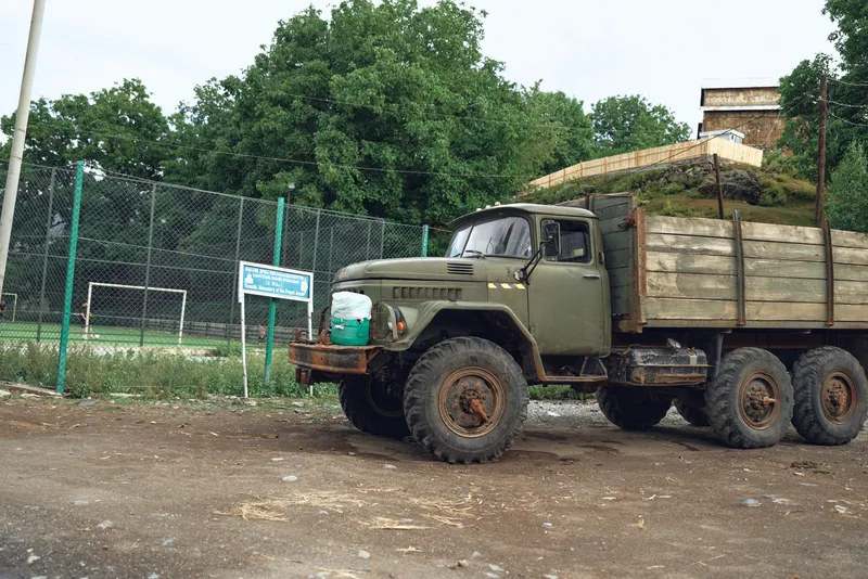 Промышленное транспортное средство с загруженными бревнами стоит на грязном участке на территории лесозаготовительного предприятия, солнечный свет освещает суровый ландшафт и активную транспортную…