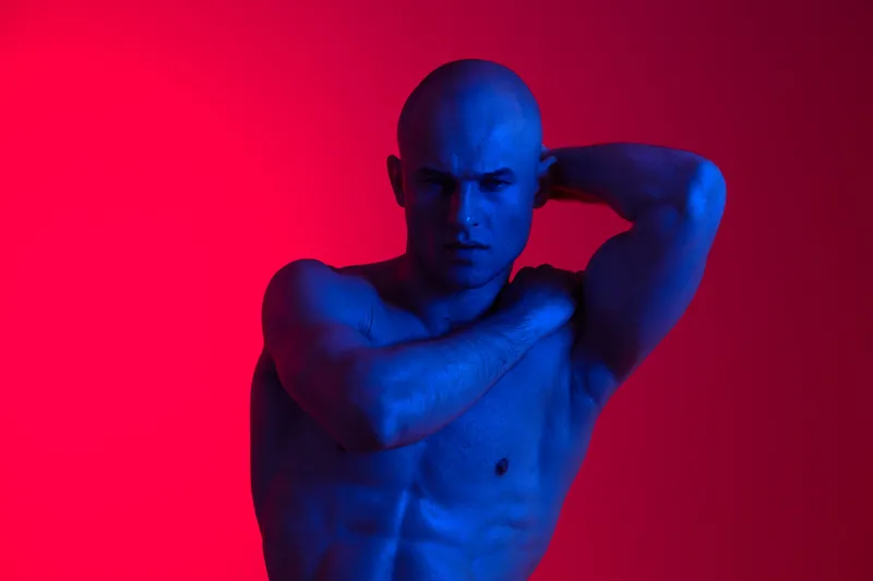 Athletic man posing with a bold expression in vibrant colors, showcasing strong muscles and dramatic lighting. Artistically illuminated against a dynamic background.
