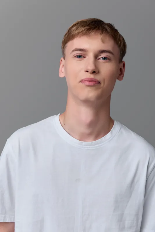Man, young, casual in white t shirt with neutral studio backdrop, relaxed expression and soft lighting, simple everyday style, unobtrusive mood for lifestyle or fashion projects