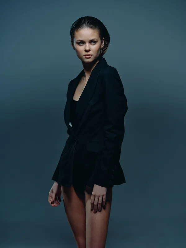 Young woman in black blazer posing confidently with dark background and moody lighting