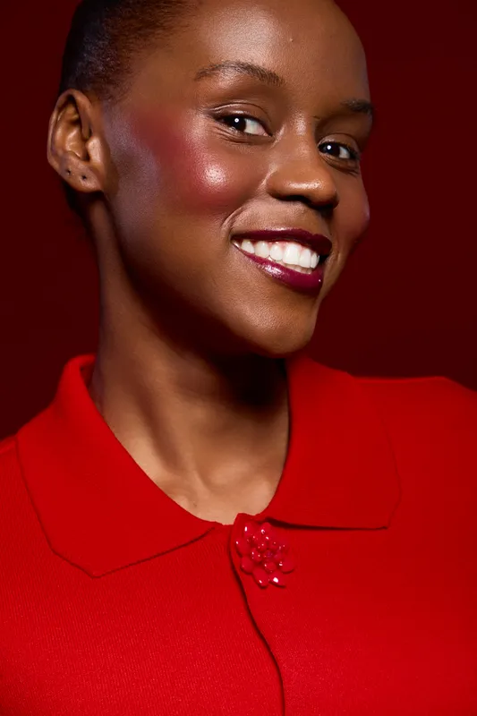 Close-up portrait of a smiling dark skinned African woman wearing a red top against a red background. Concept of beauty, confidence, fashion, and elegance in studio lighting.