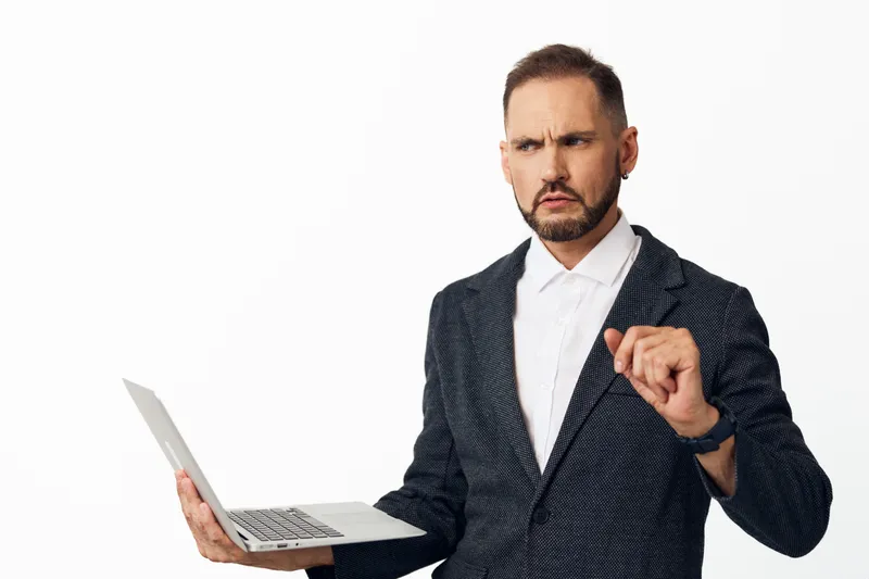 A corporate professional man on an isolated colored backdrop, holding a laptop and showing intense focus, determination, and confidence, capturing a moment of proactive business engagement.