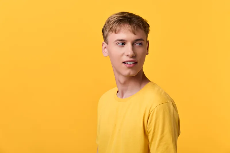 Young man in a yellow shirt stands before a vibrant yellow background, studio lighting highlights casual fashion and a relaxed pose, clean composition, warm mood for lifestyle and creative projects