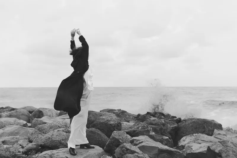 couple dancing on rocky shoreline, sea breeze and silhouette against a cloudy sky, black and white scene highlighting motion, romance and freedom in outdoor style
