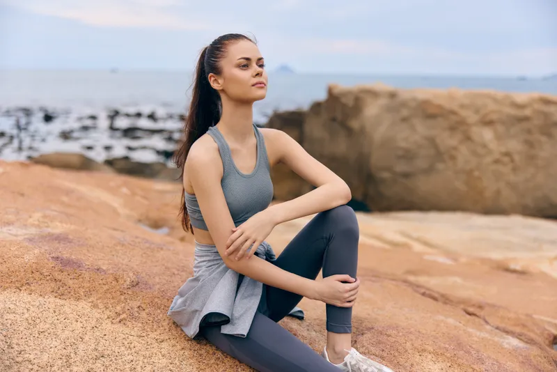 Fit young woman practicing mindfulness on rocky beach, wearing athletic wear, enjoying nature, embodying wellness and serenity, perfect for health and fitness concepts