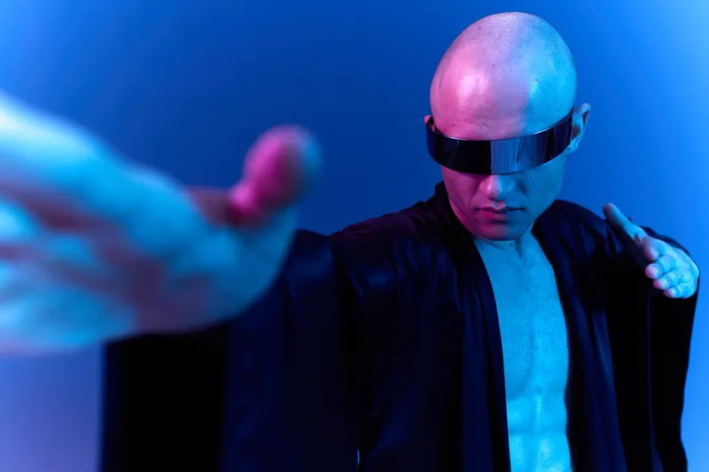 A man in futuristic attire, wearing sleek sunglasses, poses dramatically with a powerful expression. The image features vibrant colors, creating an intense atmosphere.