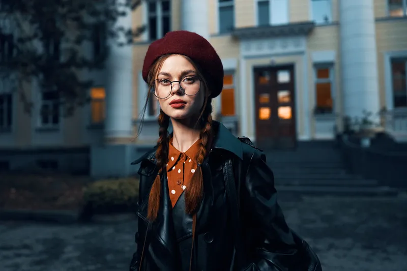 Модная женщина в красном берете и очках уверенно позирует на фоне исторического здания на городской улице