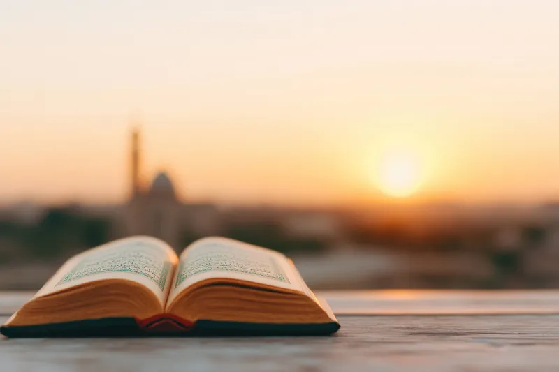 Открытая священная книга, лежащая на деревянной поверхности на закате, передает духовность и умиротворение, с теплой цветовой палитрой, мягким боке и безмятежным городским пейзажем на заднем плане