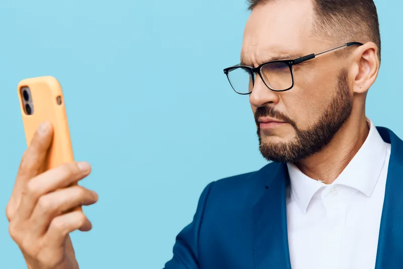 A focused business professional man stands against a vibrant colored background, expressing confidence, determination, and calm focus as he reviews notes on his smartphone.