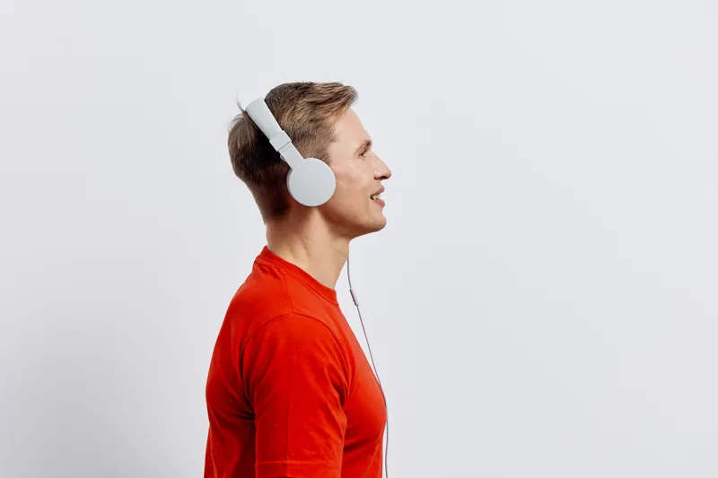 smiling man wearing white headphones in red shirt listen music isolated on plain light background digital detox concept wellness mental health relaxation