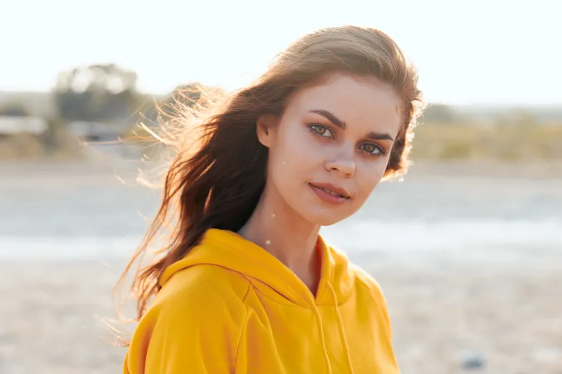 Женщина в желтой толстовке наслаждается ветреным днем на пляже, ее волосы развеваются на ветру