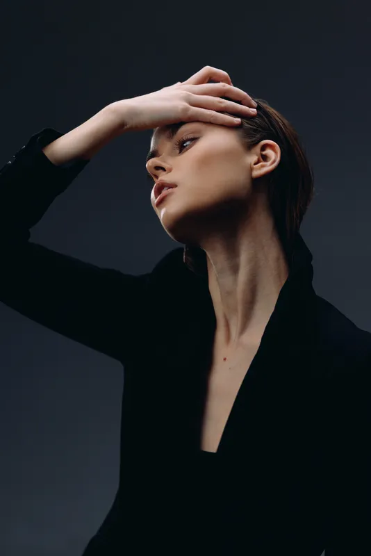 Elegant woman in black clothing posing with raised hand against dark background, showcasing beauty and style.