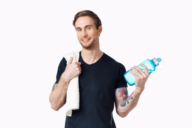 Мужчина в черной футболке с бутылкой воды в руке и полотенцем на плече, кадрированный вид