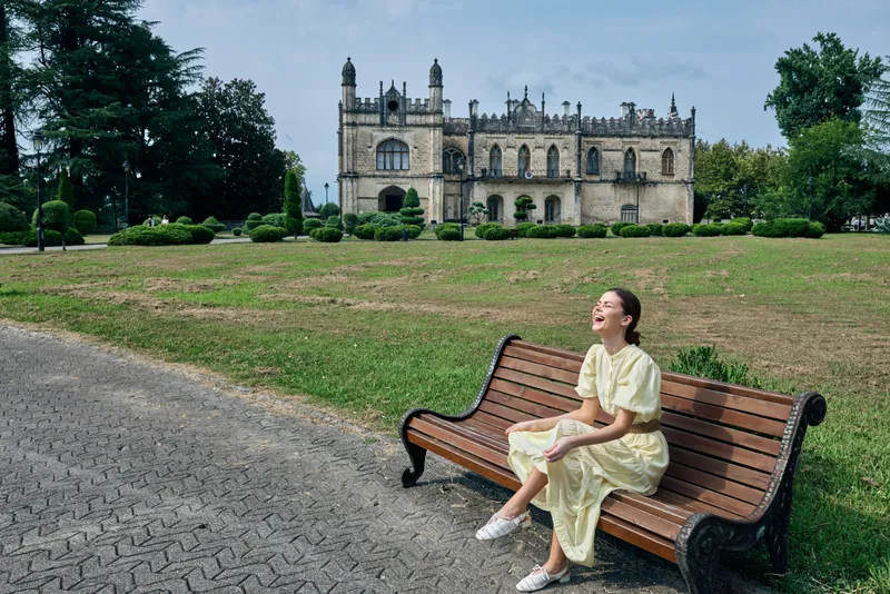 woman on bench in park with historic building background smiling and relaxed authentic inclusive portrait showing leisure and happiness in green public space with classic facade