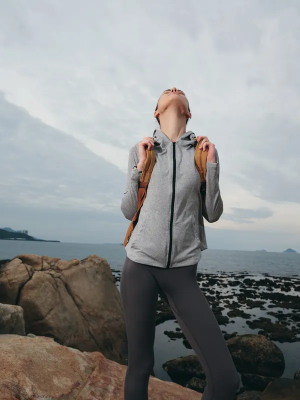 Young woman in athletic gear poses on rocky shoreline, showcasing outdoor lifestyle, fitness, and adventure, with natural scenery and overcast skies