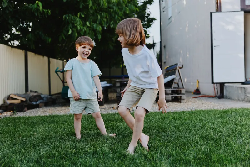 Two cheerful children playing in a sunny garden, showcasing joy and laughter in a lush green setting. The scene captures the essence of childhood innocence and fun.