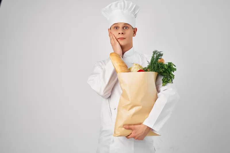 Весёлый мужчина-шеф-повар с пакетом продуктов работает на кухне