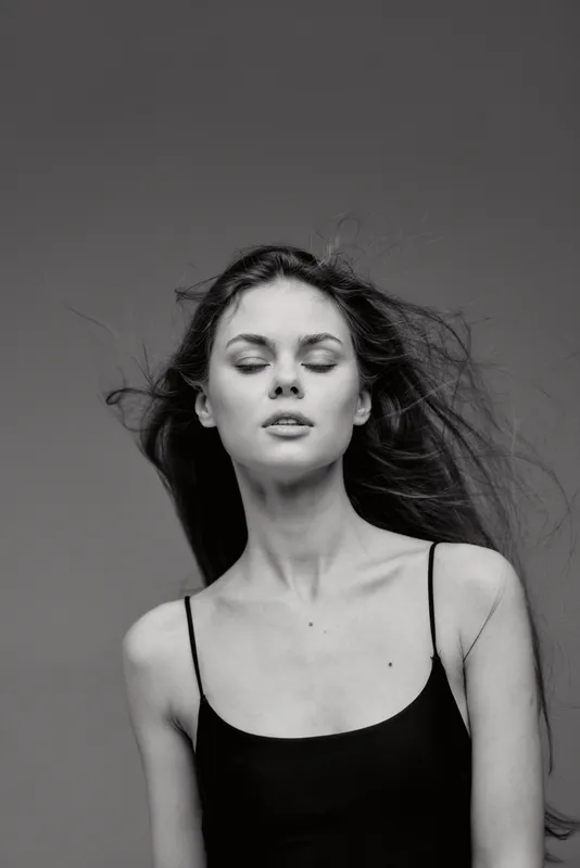 Black and white portrait of a calm woman with closed eyes wearing a black top against a plain background