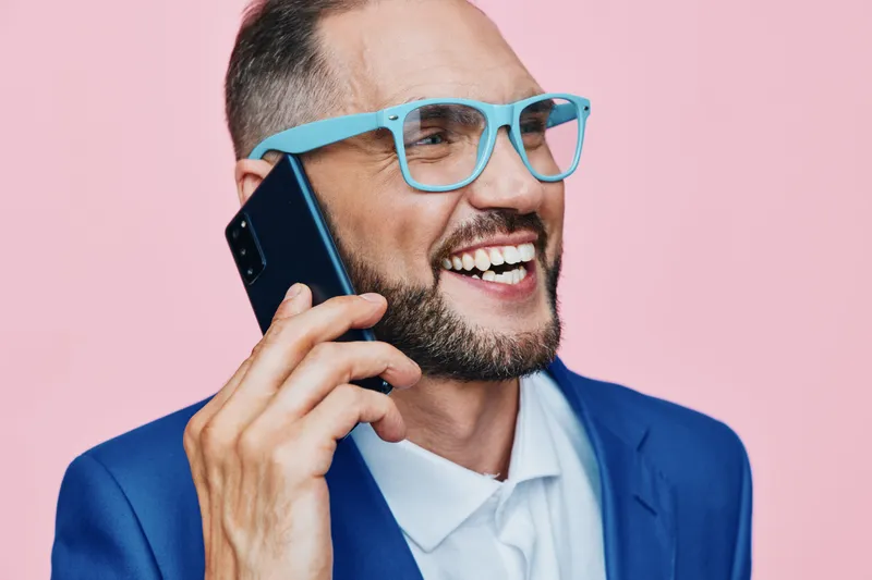 A professional man in a sharp blue suit talks on the phone, exuding confidence and positive energy. The isolated colored background highlights a modern business vibe.
