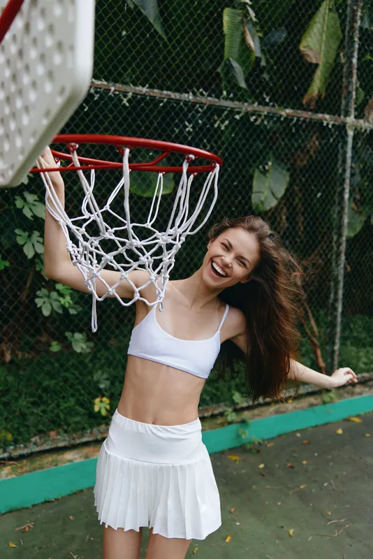 Cheerful young female basketball player in white sportswear enjoying sports on a court surrounded by greenery Capturing the joy of athletic expression and vitality