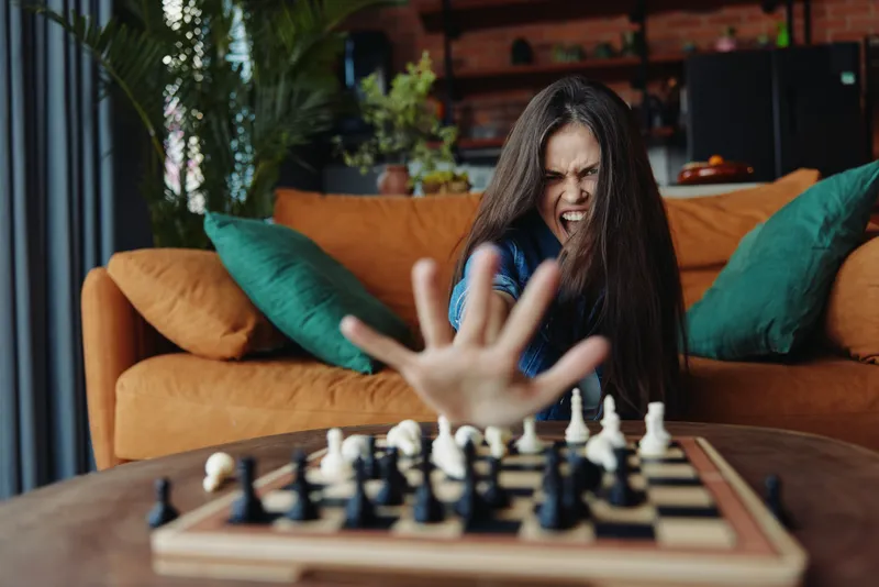 Женщина играет в шахматы, сидя на диване