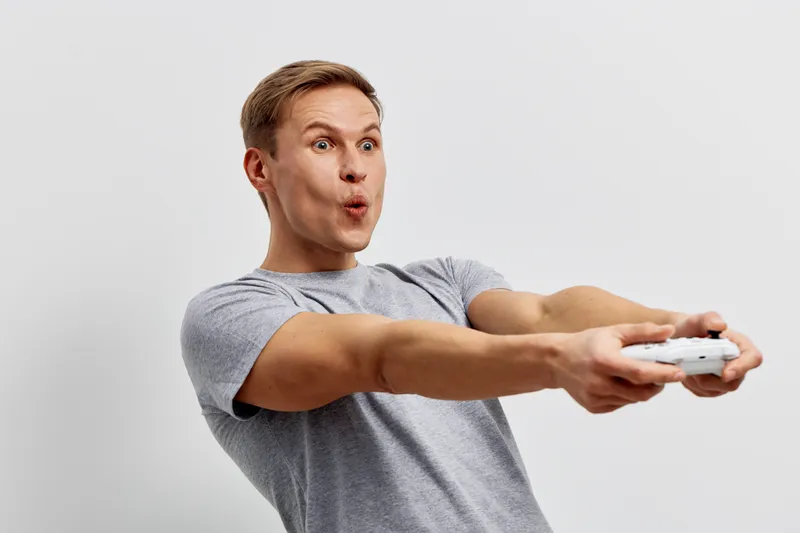 surprised caucasian man wearing gray t-shirt holding game controller playing video games excited emotion isolated on light background digital entertainment concept