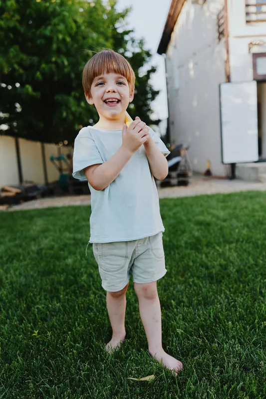 Happy boy playing outdoors, enjoying a sunny day in the garden, wearing light clothing and standing on green grass, radiating joy and innocence.