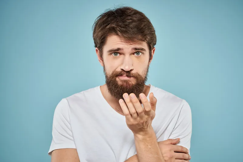 Бородатый мужчина в белой футболке, эмоции, образ жизни, жестикуляция руками на синем фоне