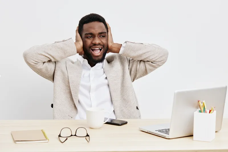 Happy cheerful man wearing casual sweater enjoying listening music with headphones while sitting at a desk with laptop and stationery, white background, studio shot, lifestyle concept, positive mood.