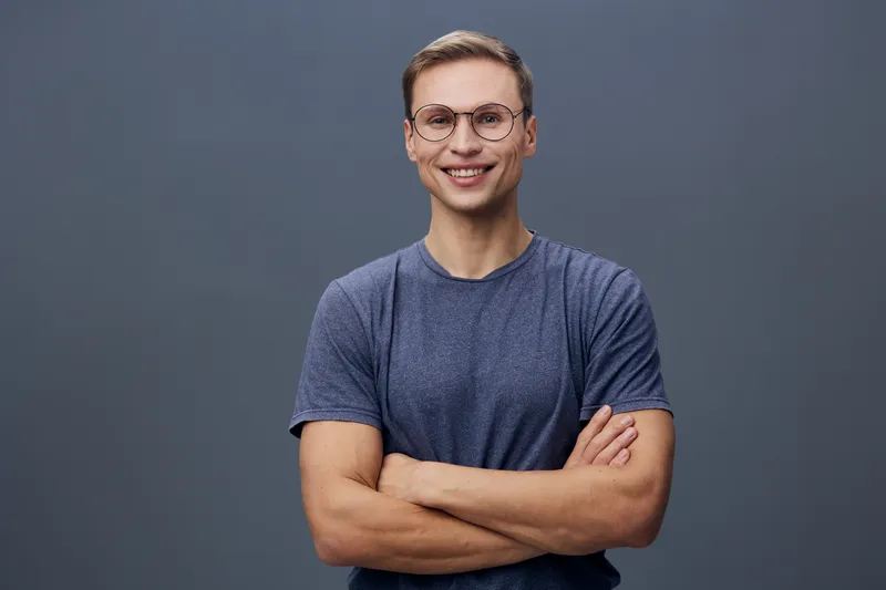 Smiling young caucasian man wear glasses blue tshirt arms crossed look camera isolated gray background digital detox mental health concept