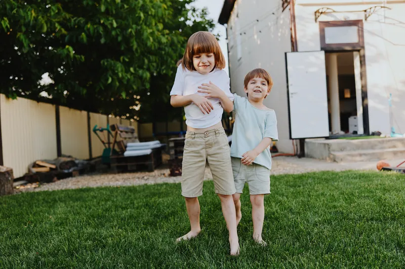 Happy children playing outdoors, enjoying a sunny day in the backyard, surrounded by green grass and warm sunlight, smiling and laughing together.
