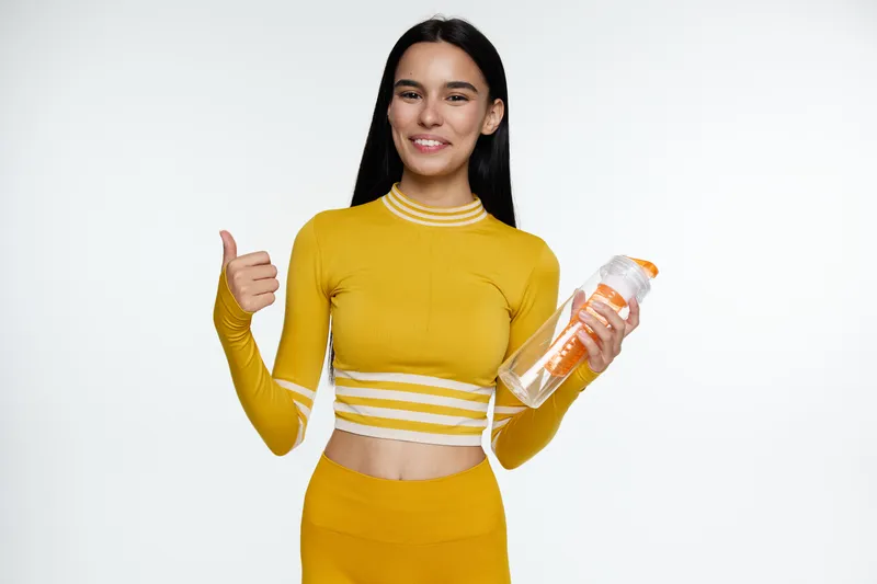 woman sport fitness wearing yellow activewear, smiling with water bottle, showing thumbs up, healthy lifestyle and exercise motivation, white background