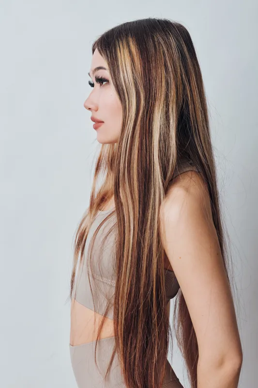 Young woman with long straight hair and natural makeup in neutral outfit posing in profile on plain background. Beauty, fashion, and casual style concept with serene expression.