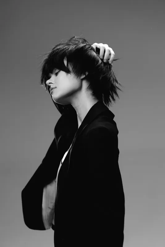 Black and white portrait of a woman with short hair wearing a blazer, expressing calm and introspective mood against a plain background.