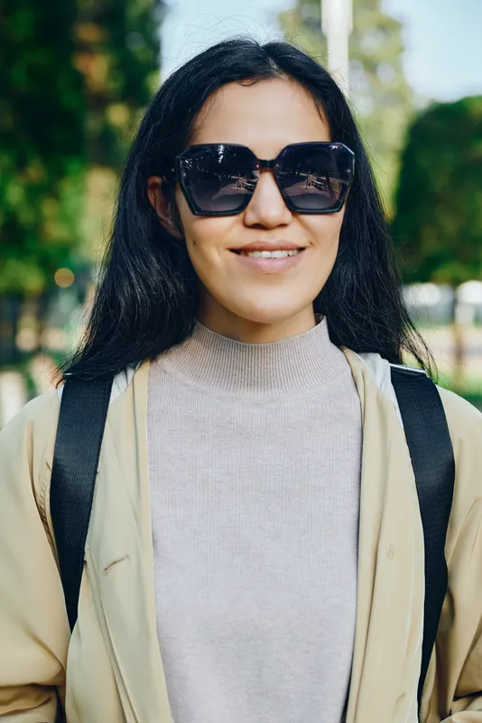 Sunglasses wearing woman outdoors smiling in casual fashion style on a sunny day in a park, showcasing confident lifestyle and relaxed elegance with minimal backdrop