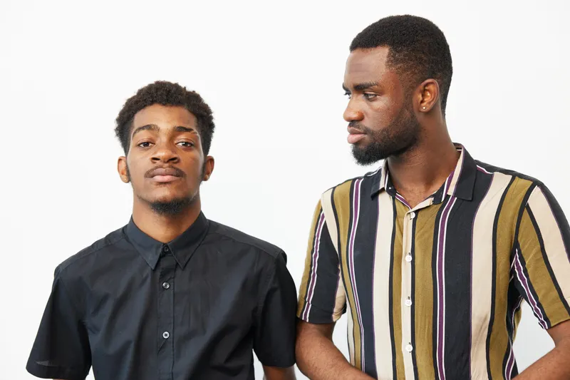Two black men standing together, showcasing friendship and positive vibes with fashionable outfits and confident expressions, ideal for lifestyle imagery.