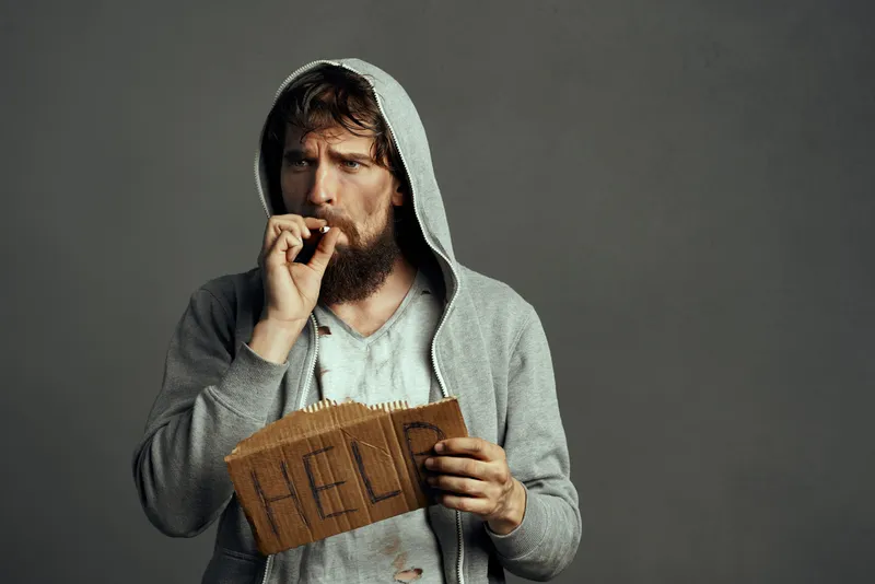 Бородатый мужчина в капюшоне с табличкой помощи на сером фоне