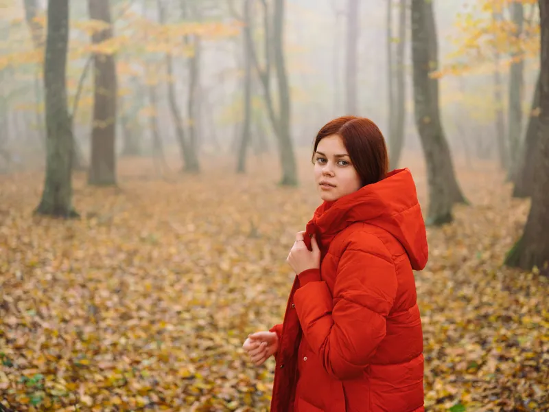 Женщина в красной куртке в лесу осенью