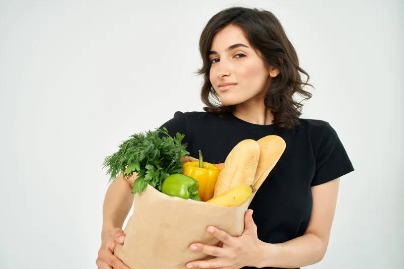 Веселая женщина с пакетом продуктов на кухне, здоровая пища и домашние дела