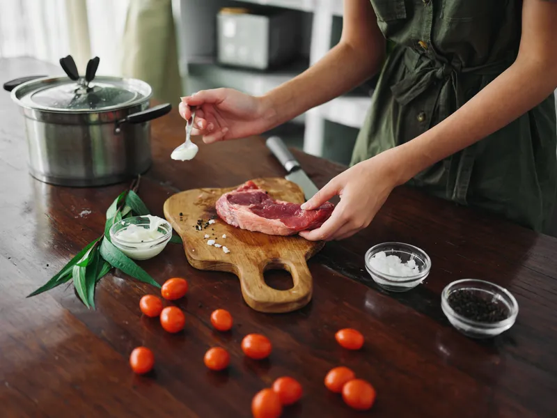 Женщина на кухне готовит ужин из мяса, овощей и специй на деревянном столе на фоне стильной кухни, крупным планом руки, образ жизни