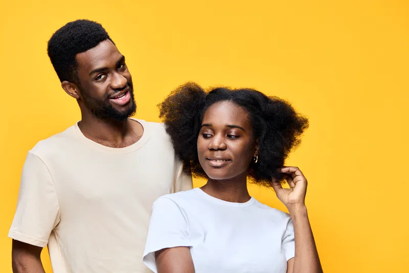 Happy couple standing against a bright yellow background, showcasing their natural hair and joyful expressions, depicting love and connection